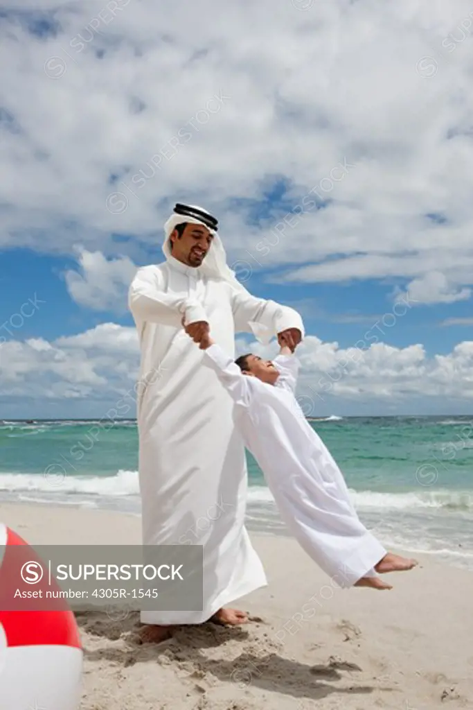 Arab father spinning around his son at the beach.