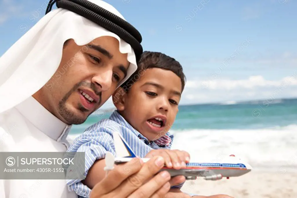 Arab father and son playing toy airplane at the beach.