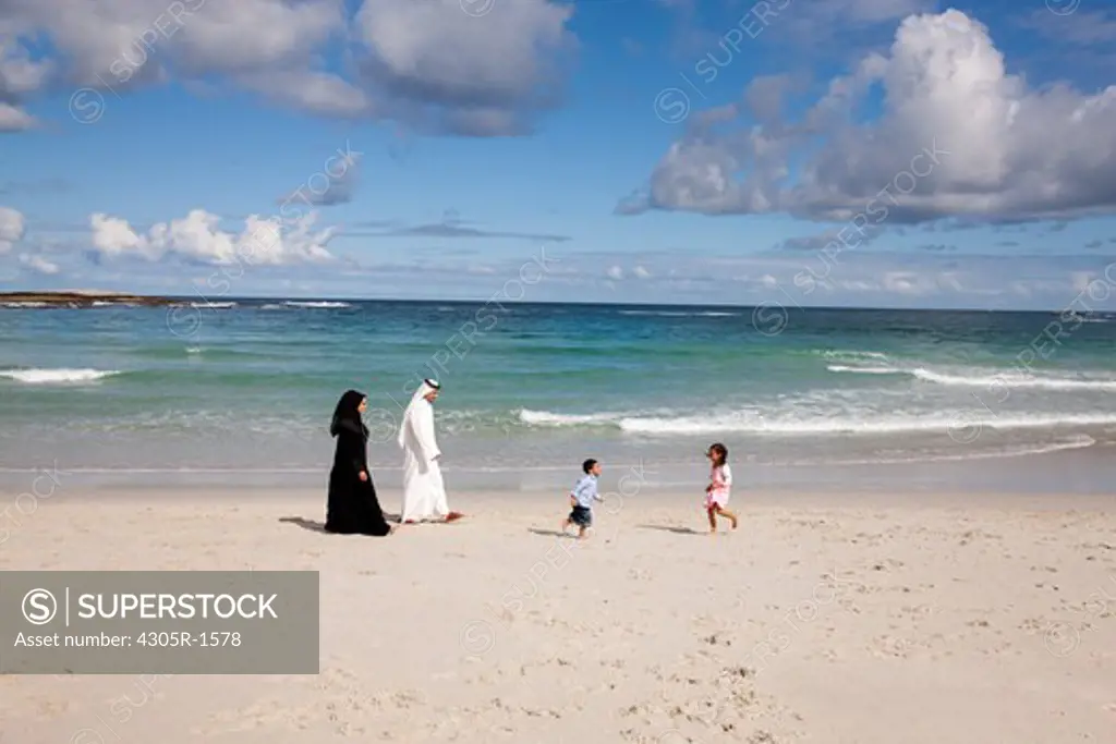 Arab family at the beach, children running on the sand.
