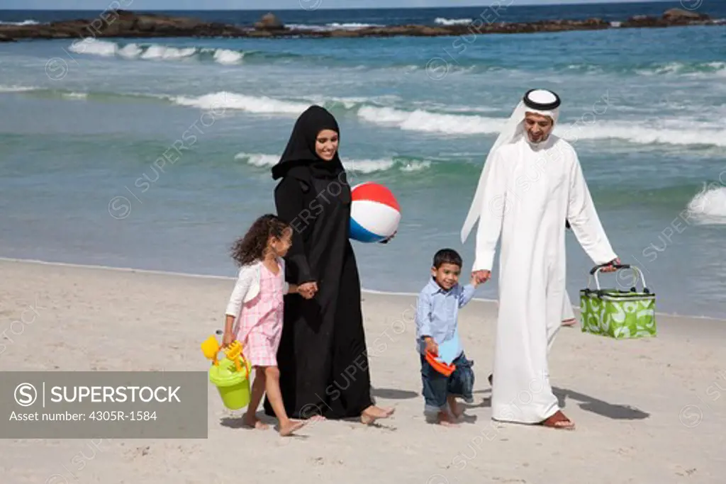 Arab family holding hands while walking at the beach.
