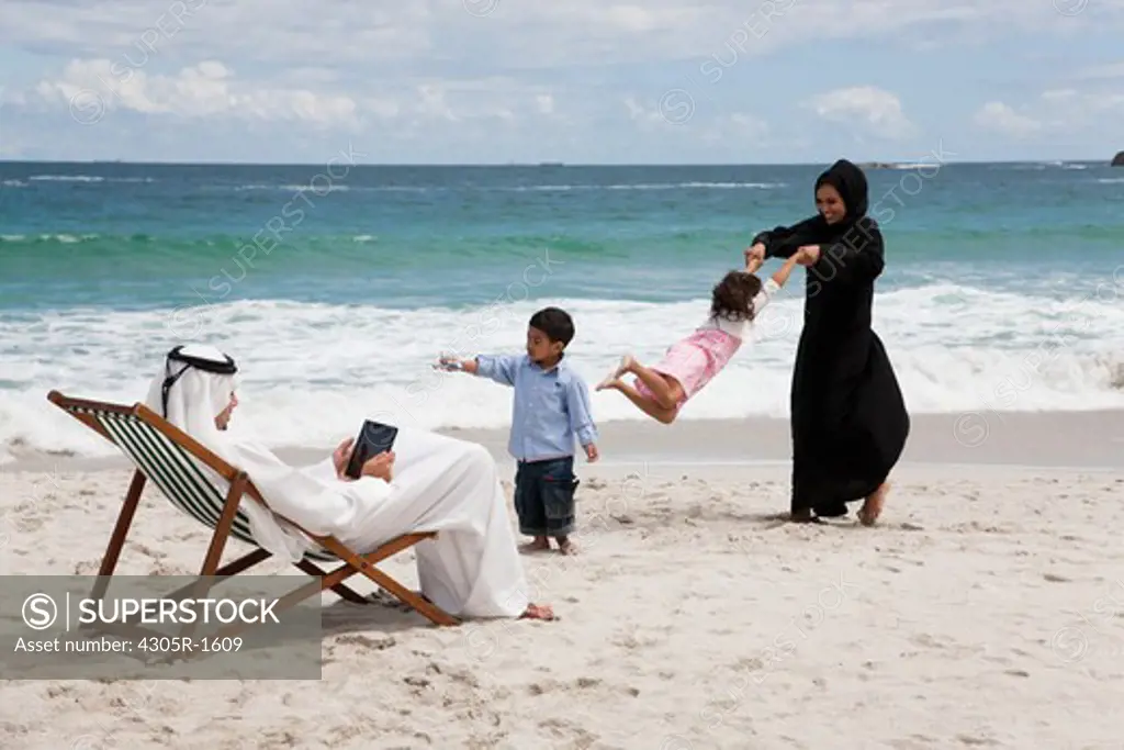 Arab family playing at the beach with father using digital tablet.
