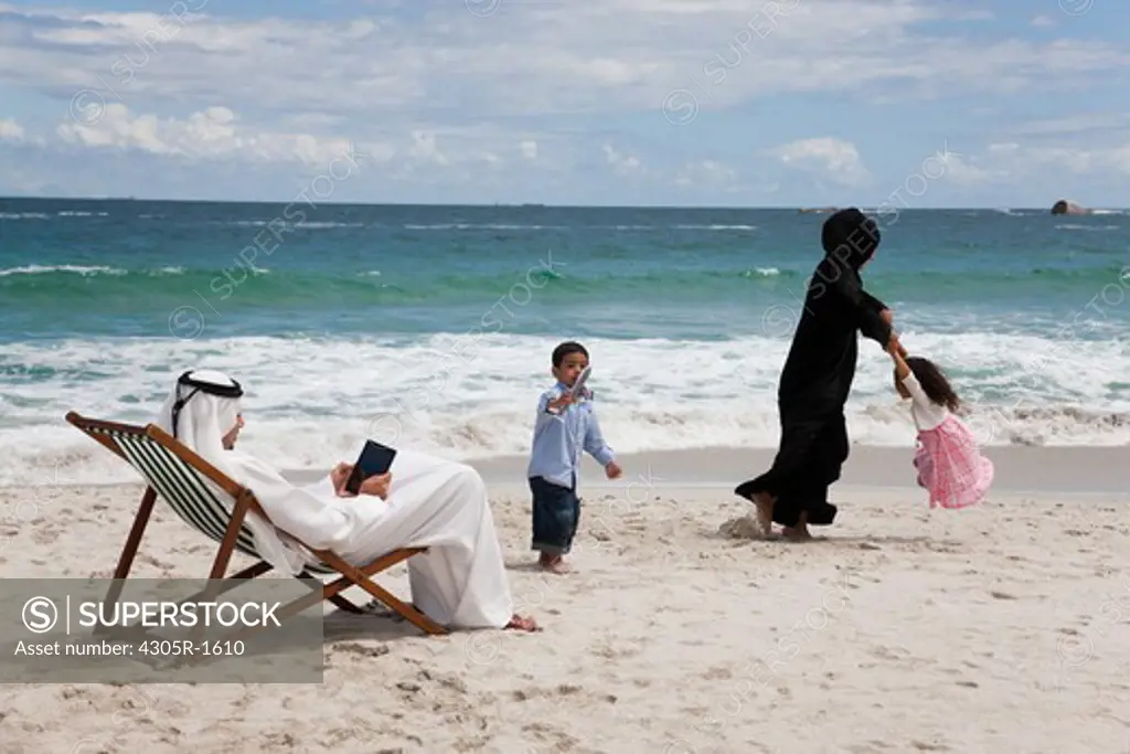 Arab family playing at the beach with father using digital tablet.