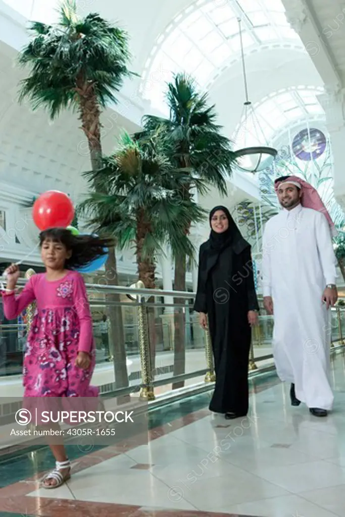 Arab family in shopping mall, girl running with balloons.