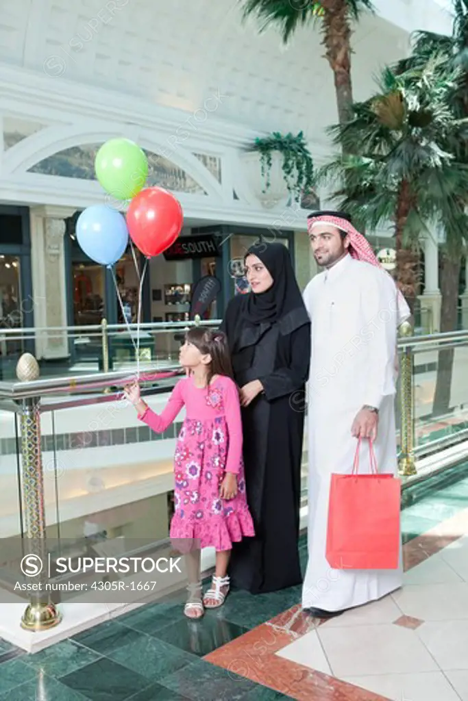 Arab family in shopping mall, girl holding balloons.