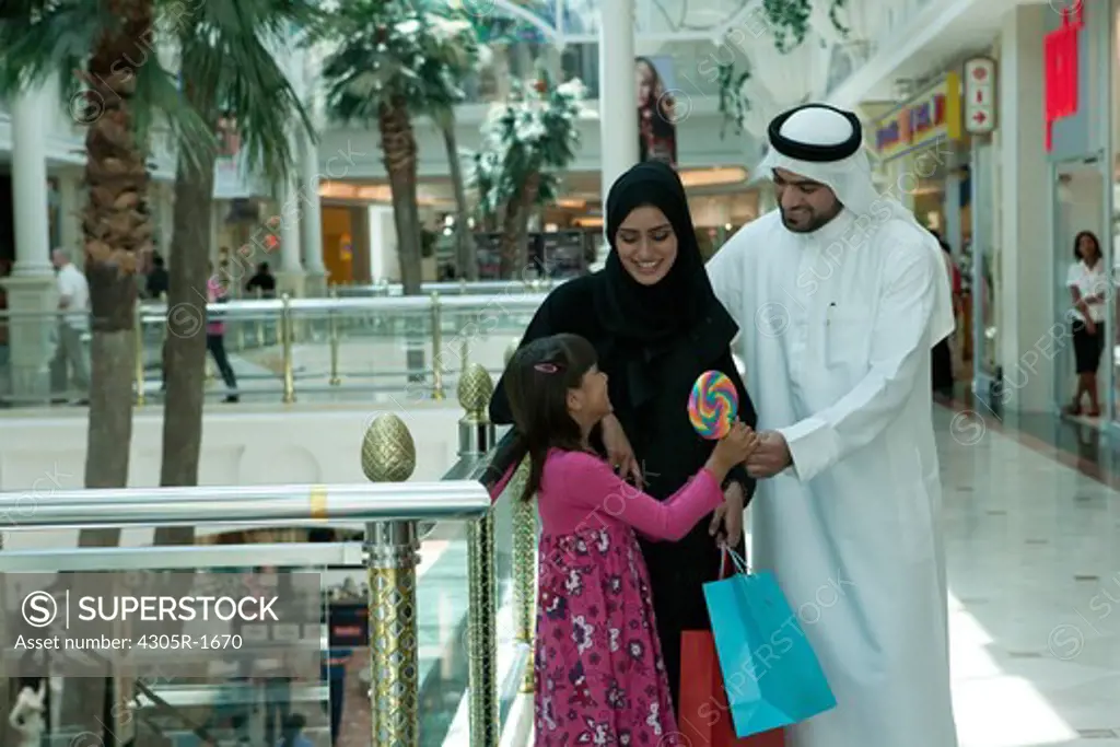 Arab family in shopping mall, father giving lollipop to his daughter.
