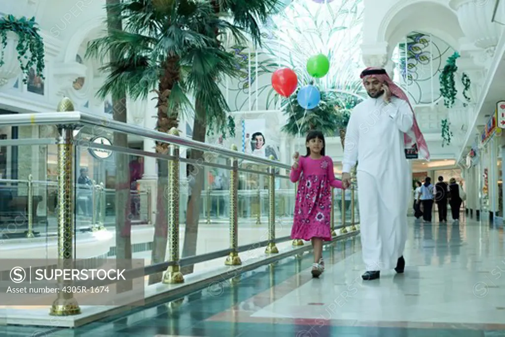 Arab father and daughter walking in shopping mall.