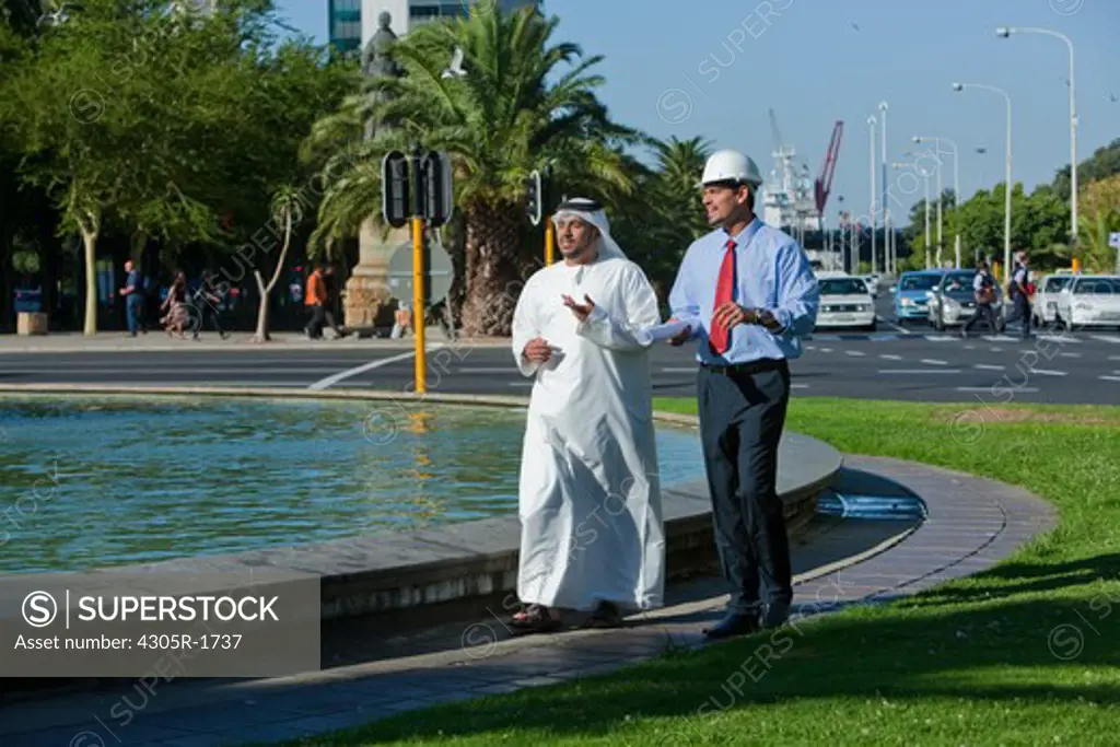Arab businessman and architect talking while walking on street.