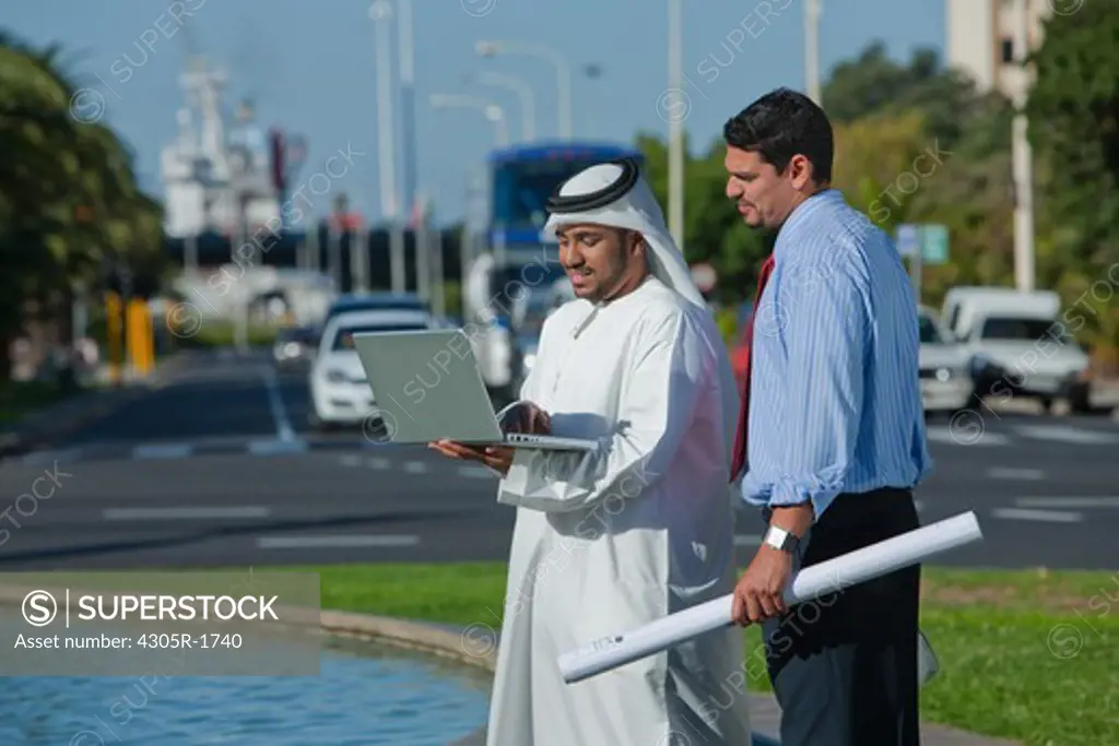 Arab businessman with laptop and architect standing on street.