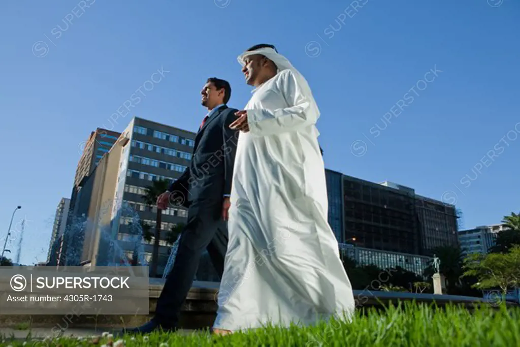 Two businessmen talking while walking at the street.