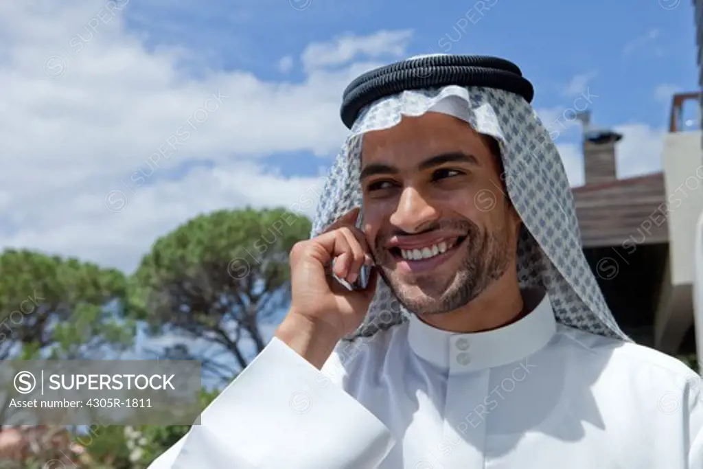 Arab man using mobile phone, standing in the balcony.