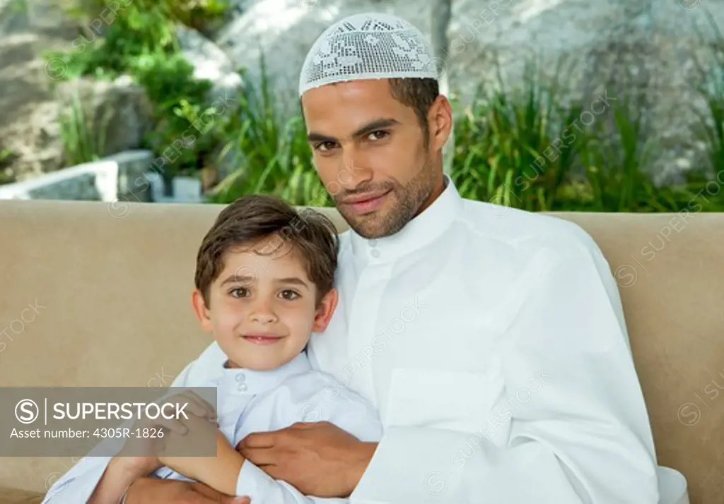 Portrait of an arab father and son sitting on sofa.