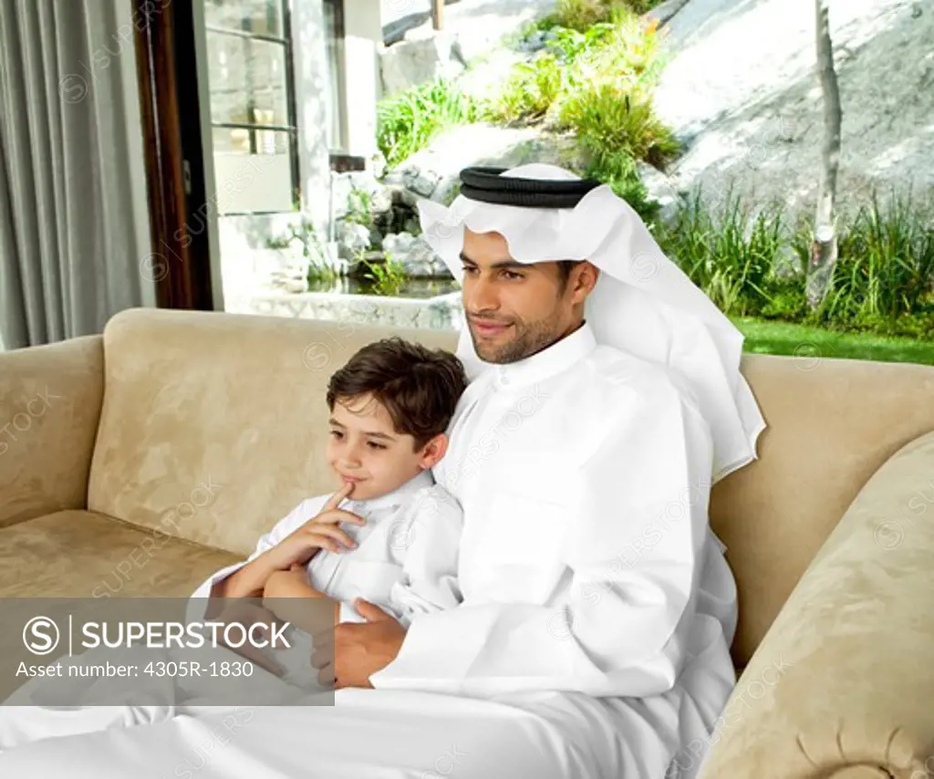 Arab father and son sitting on sofa together.