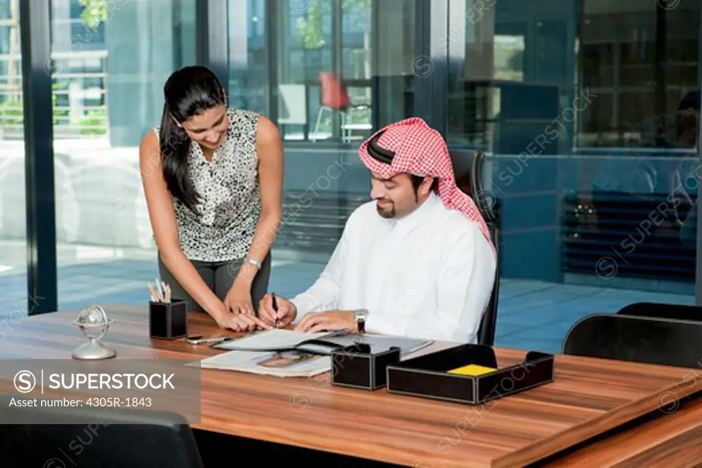 Secretary assisting arab businessman in signing documents.