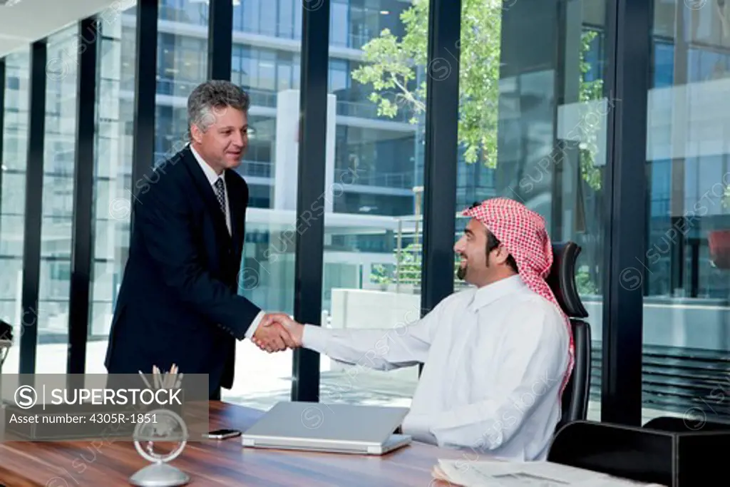 Arab businessman and western businessman shaking hands in the office.