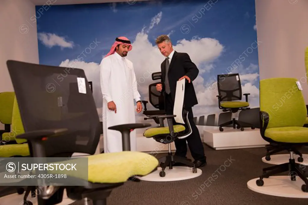 Salesman assisting arab man shopping for office chairs in furniture store.