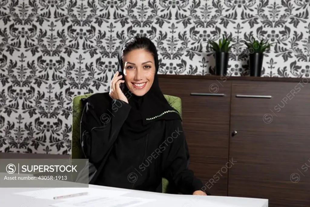 Arab businesswoman using mobile phone, smiling.