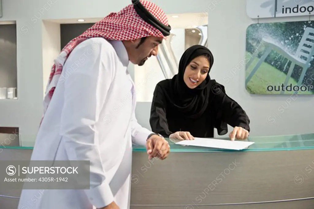Arab receptionist assisting businessman with document.