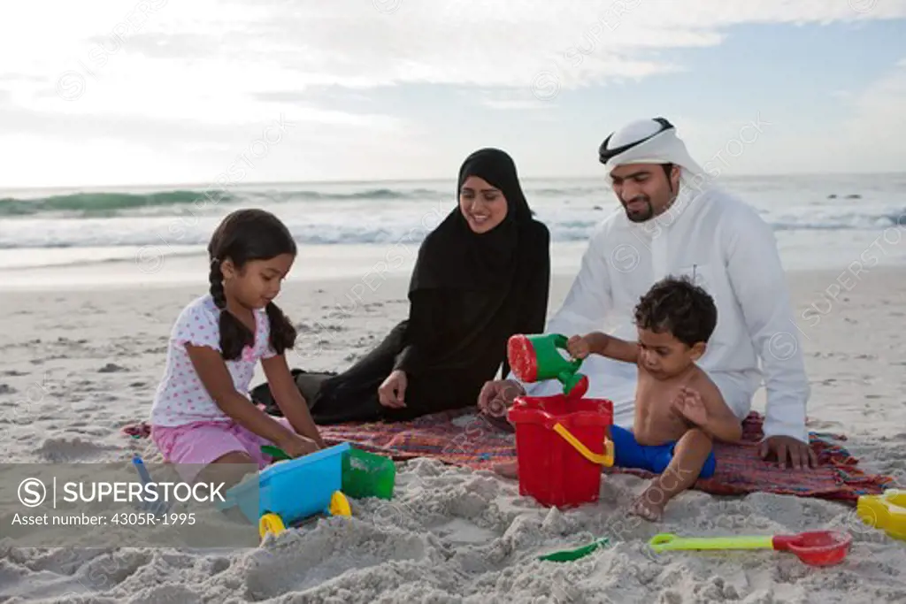 Arab family playing sand by the beach.