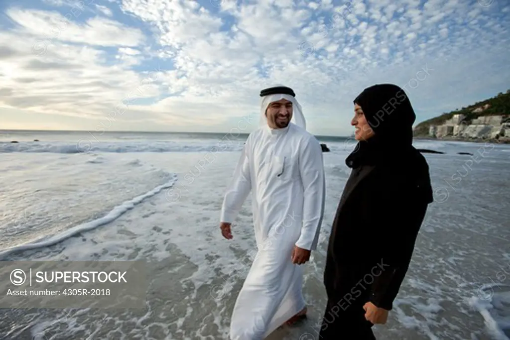 Arab couple standing by the beach, smiling.