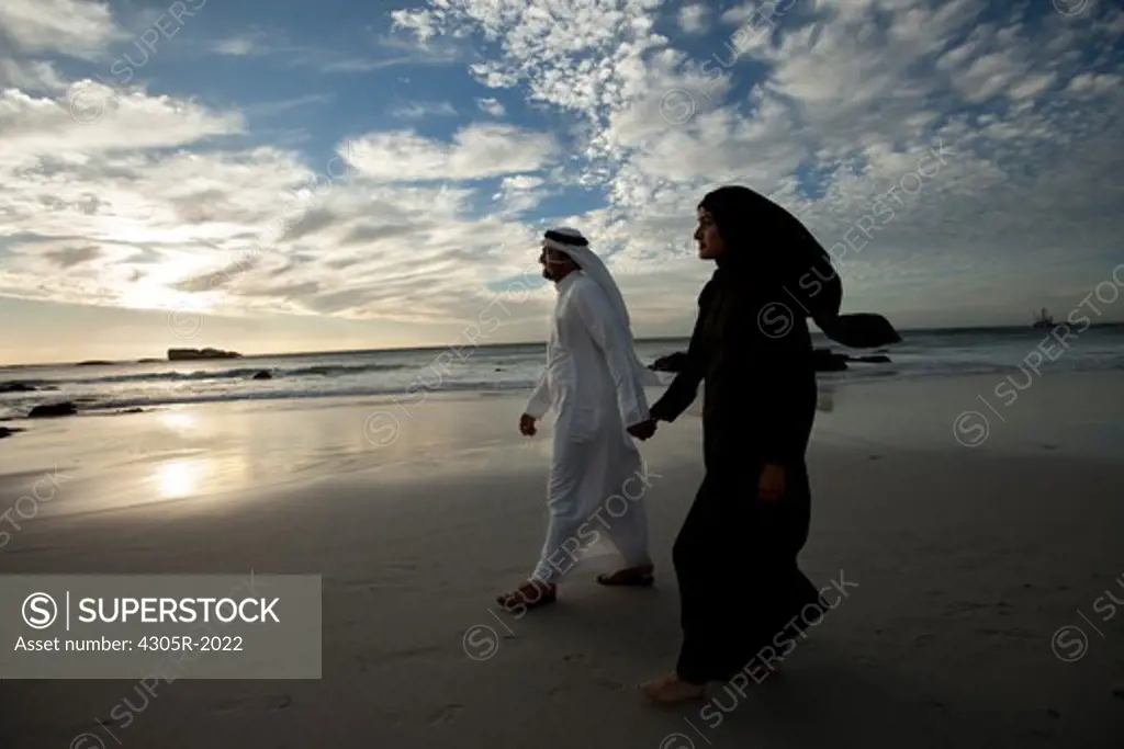 Arab couple walking by the beach, holding hands.