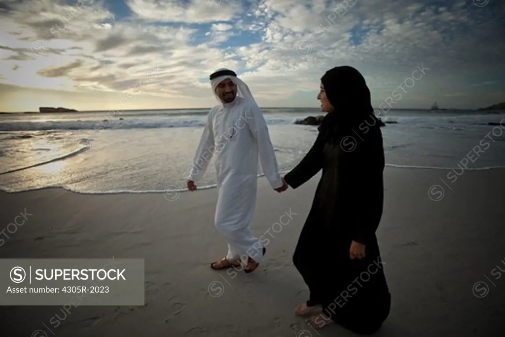 Arab couple walking by the beach, holding hands.