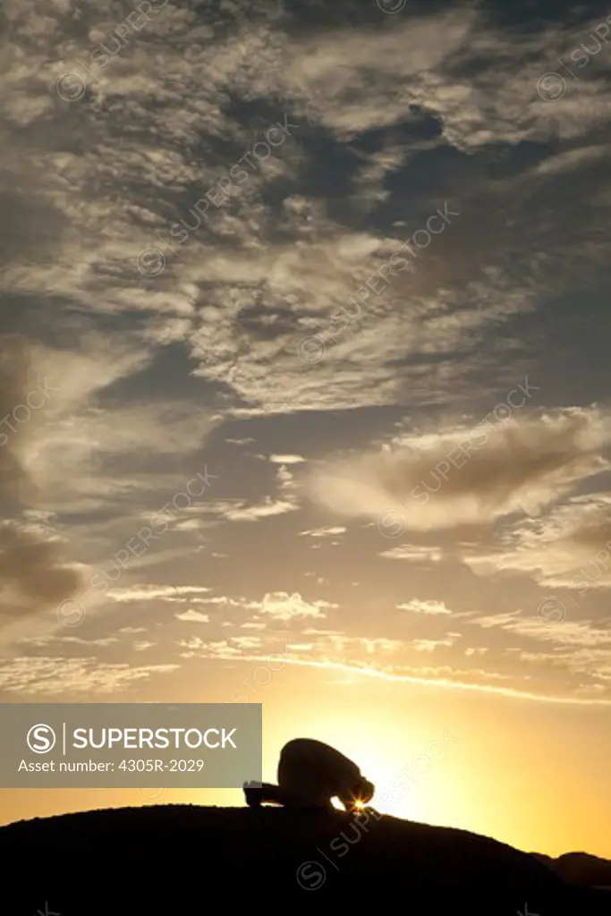 Arab man praying on the top of rock.