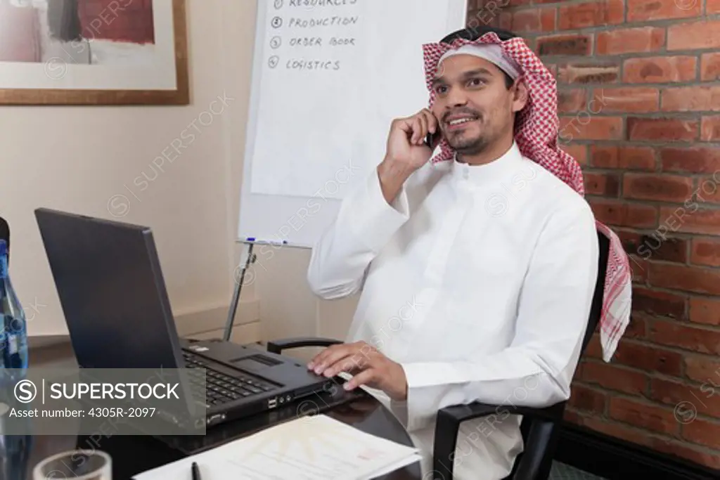 Arab businessman with laptop using mobile phone.