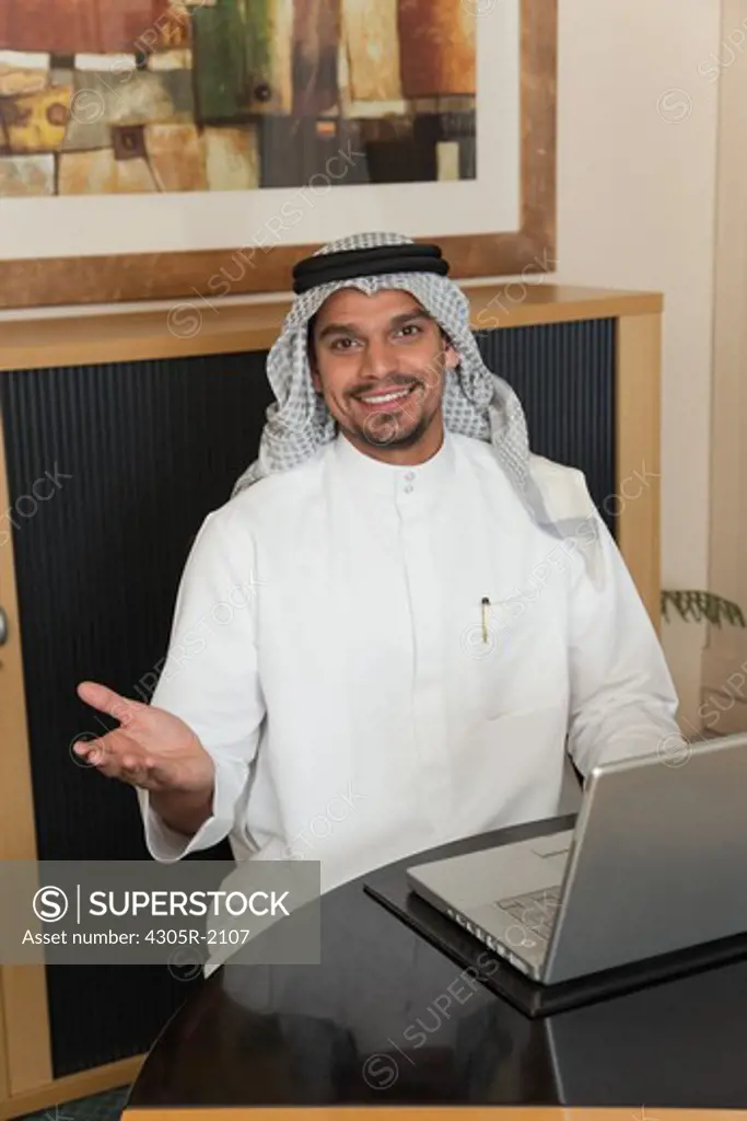 Arab businessman with laptop giving an open hand gesture.