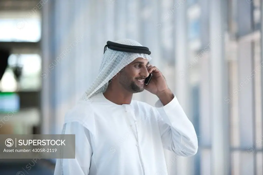 Arab businessman using mobile phone, standing by the office hallway.