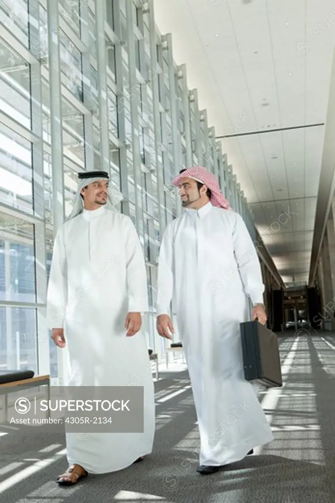 Two arab businessmen talking while walking in office hallway.