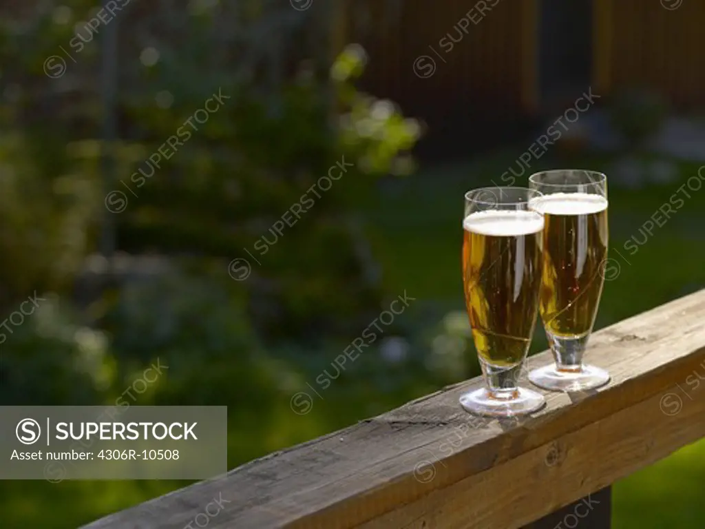 Two beer glasses on a porch banister.