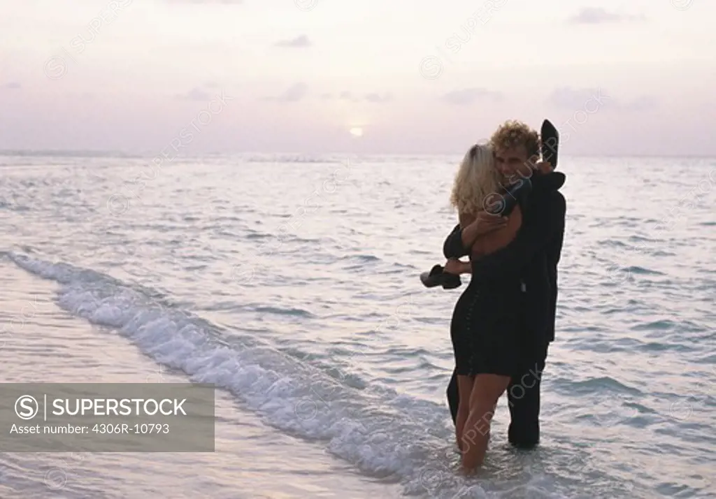 Young couple huging at the waters edge, Kuredo, Maldives.