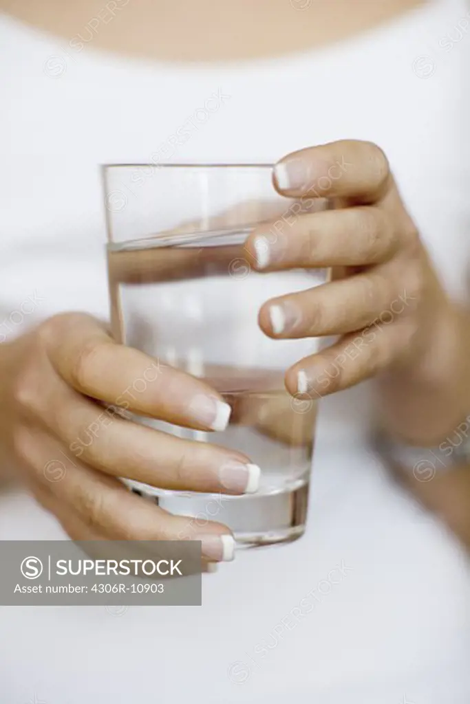 A glass of water in the hands of a woman.