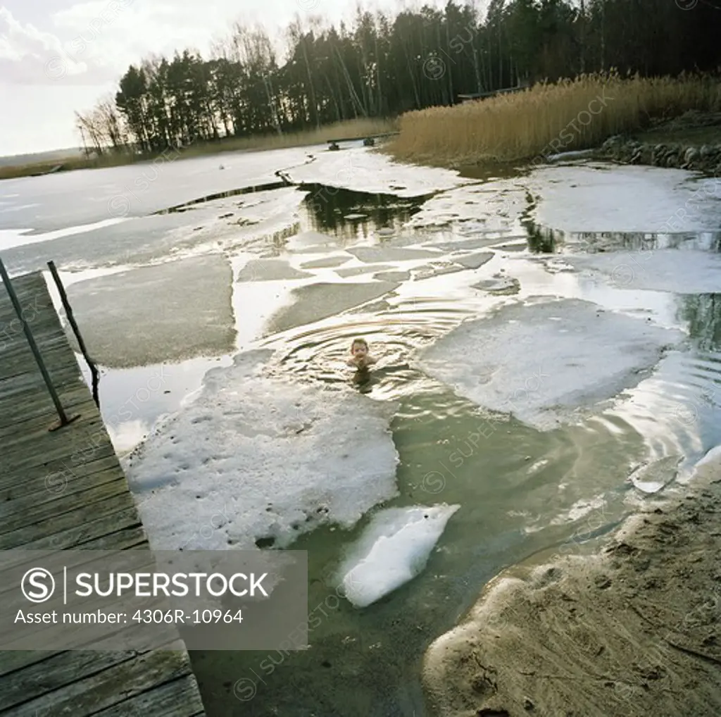 Boy swimming in cold water, surrounded by ice floe, Trosa, Sweden.