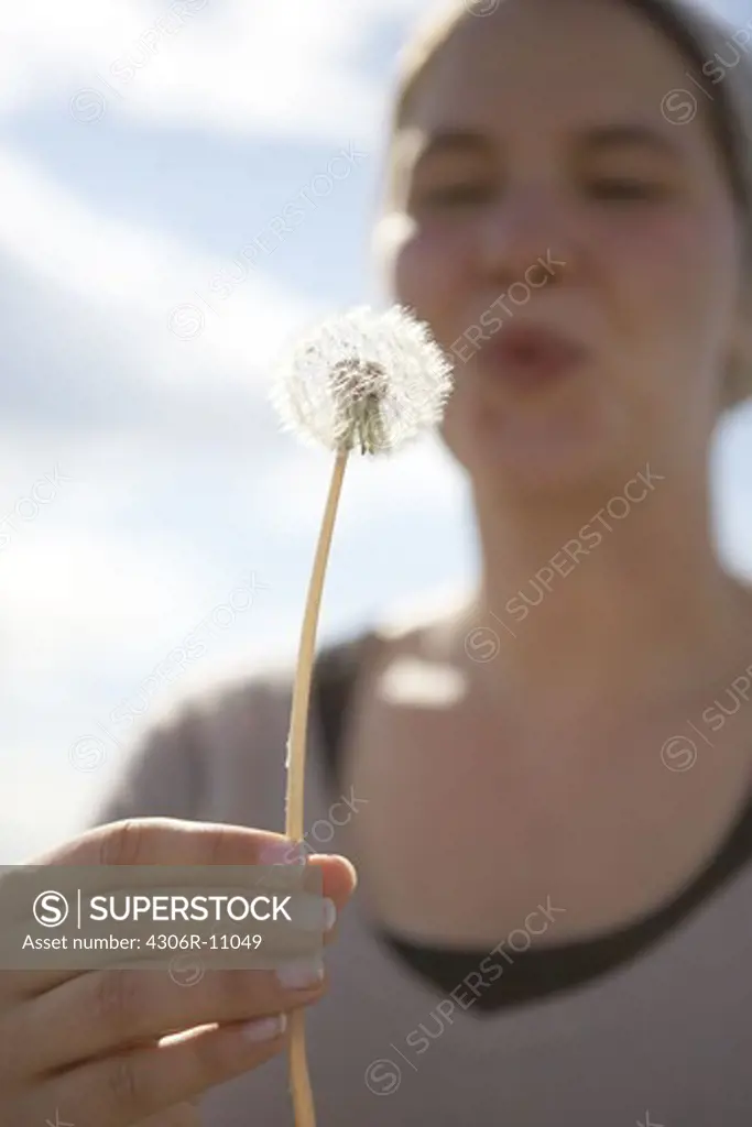 Woman holding dandelion and blowing.