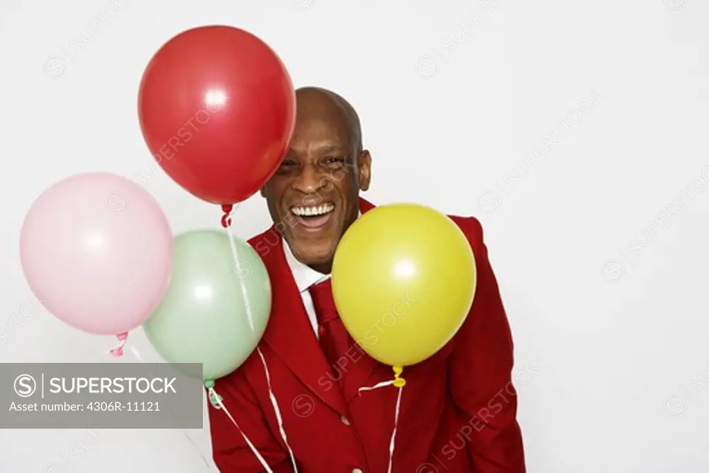 A middle-aged man wearing a red suit and holding balloons.