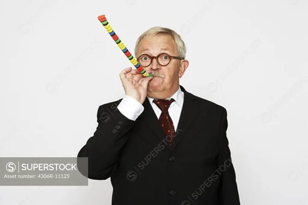 An older man in a suit blowing in a party horn blower.