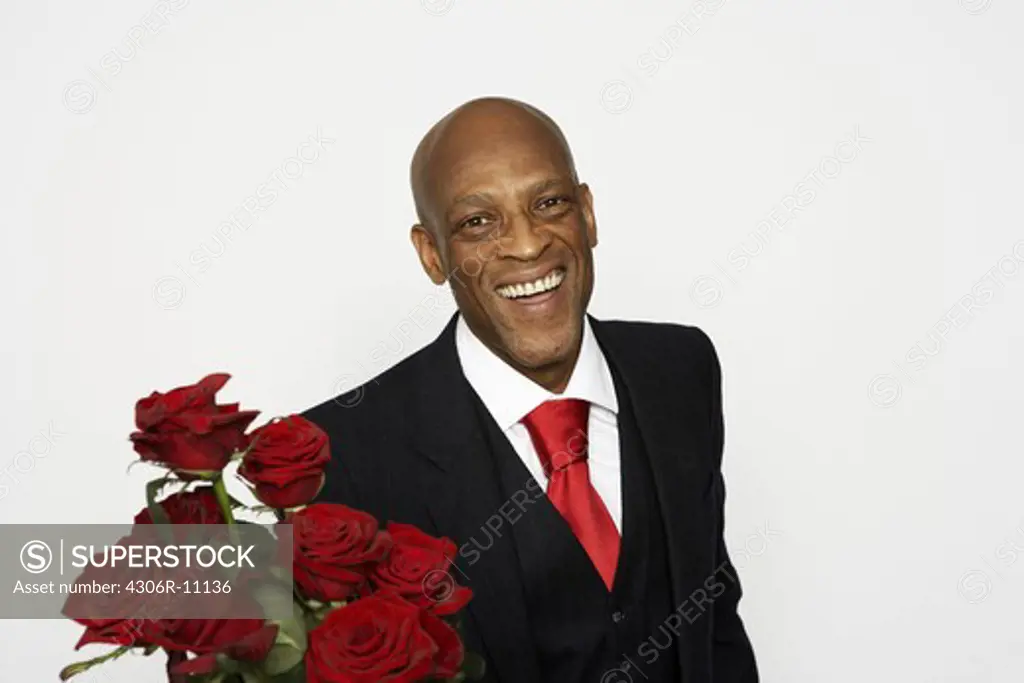A man wearing a suit and holding a buncht of red roses