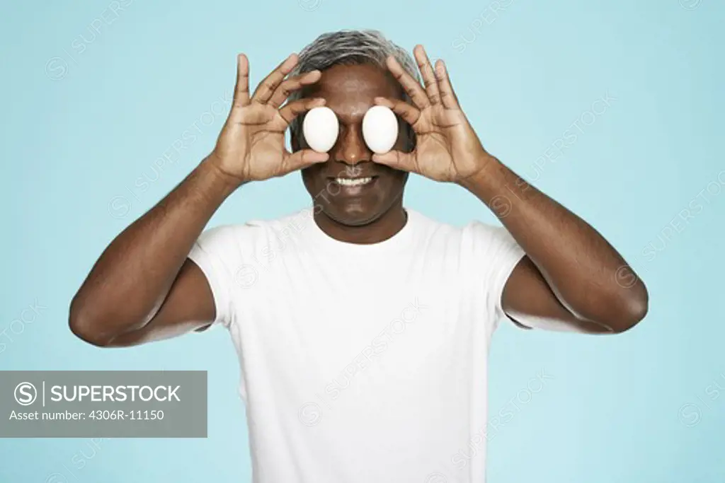 Portrait of a middle-aged man, holding eggs in front of his eyes.