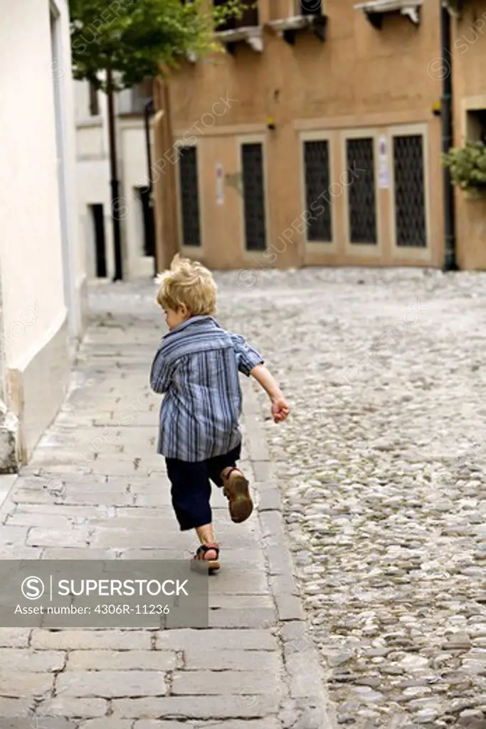 A very young boy running away from the photographer.
