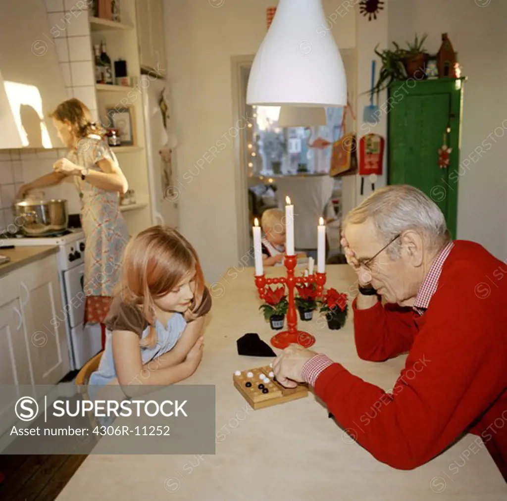 Elderly man playing a party game with a girl, woman cooking in the background, Stockholm, Sweden.