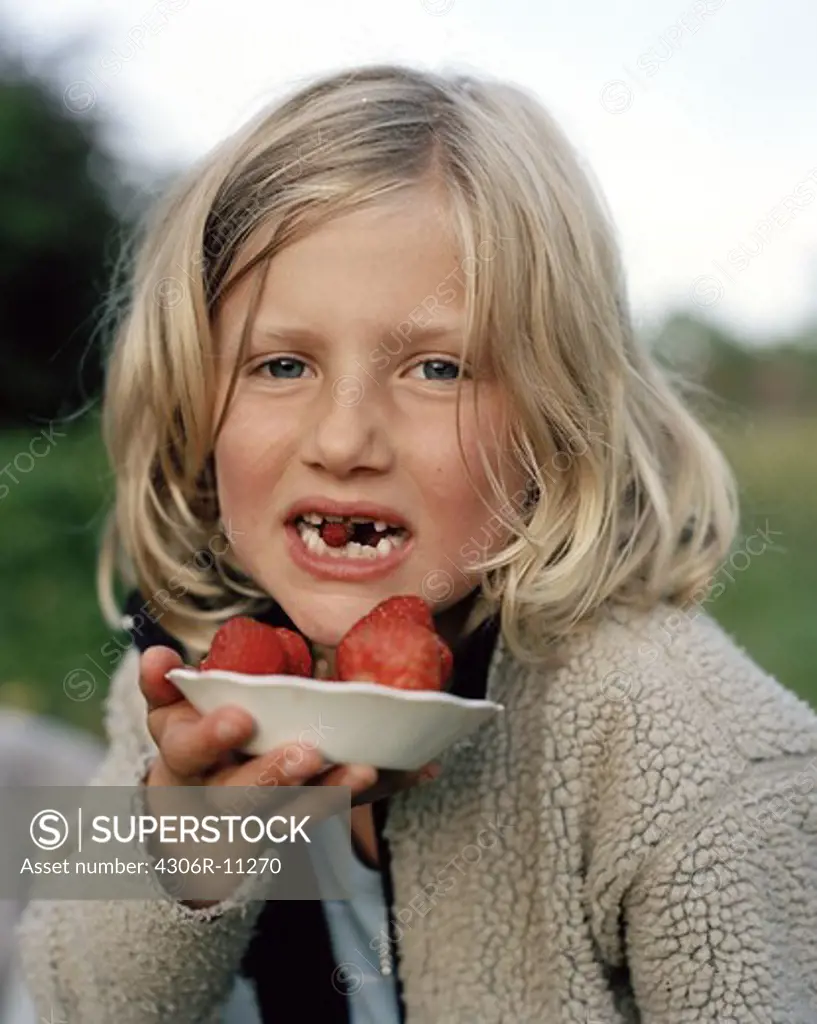 Girl with a wild strawberry between her teeth, holds a plate with strawberries, Oland, Sweden.