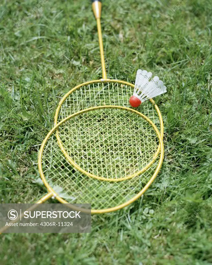 Two badminotn rackets and a shuttlecock lying on a lawn.