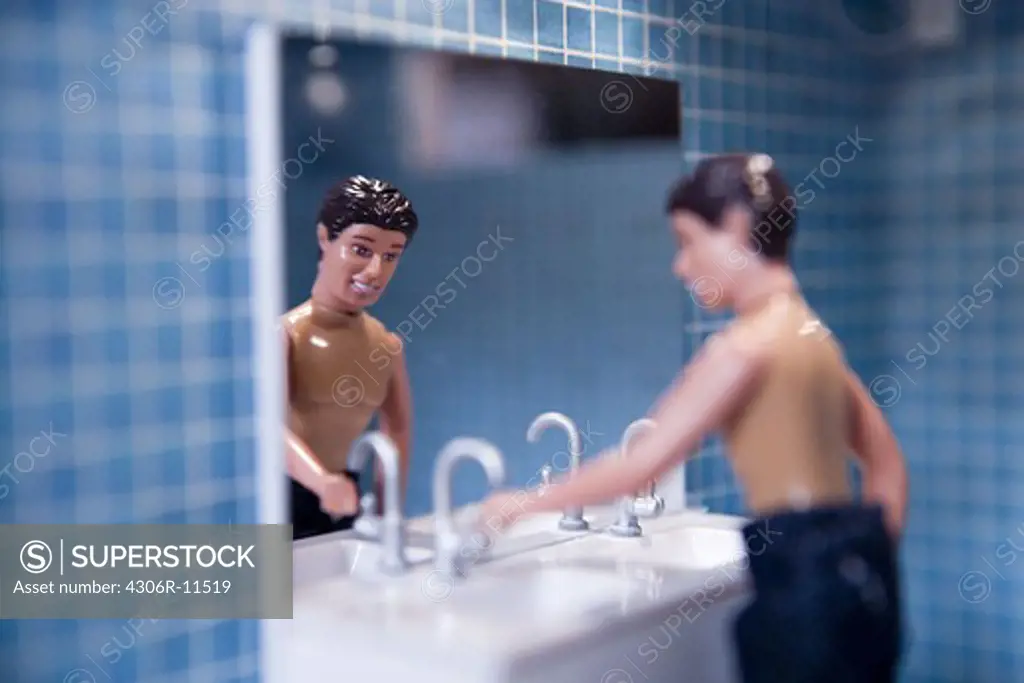 A doll standing by a handbasin in a dolls house.