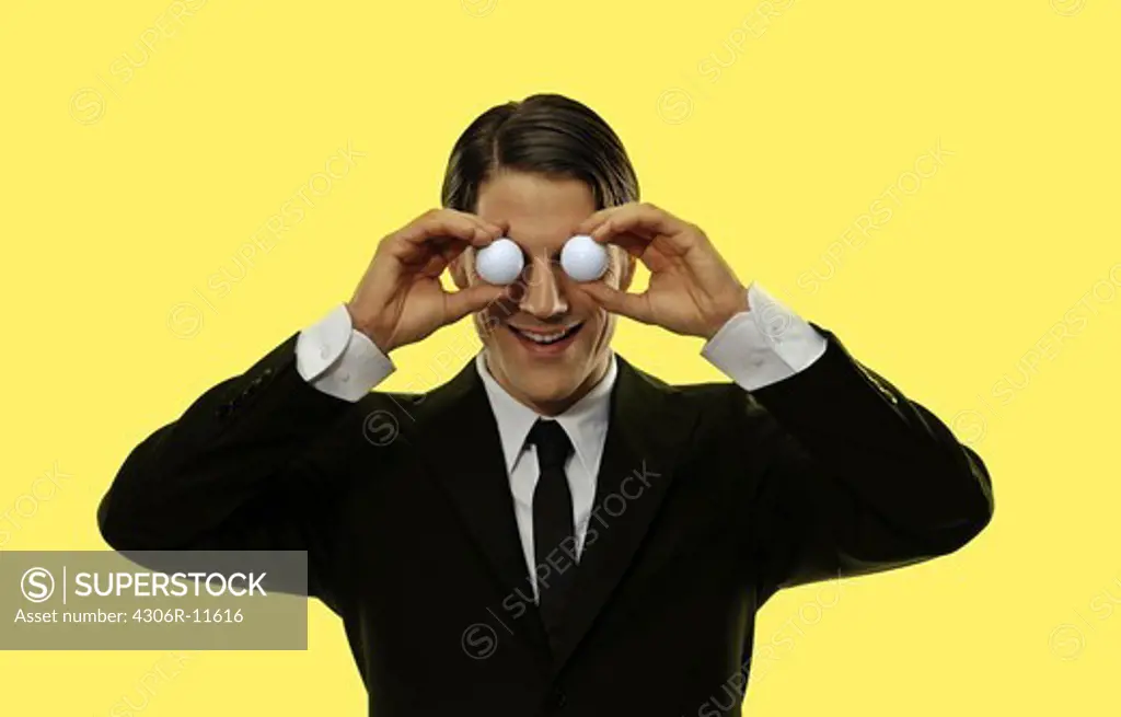 A business man holding two balls infront of his eyes.