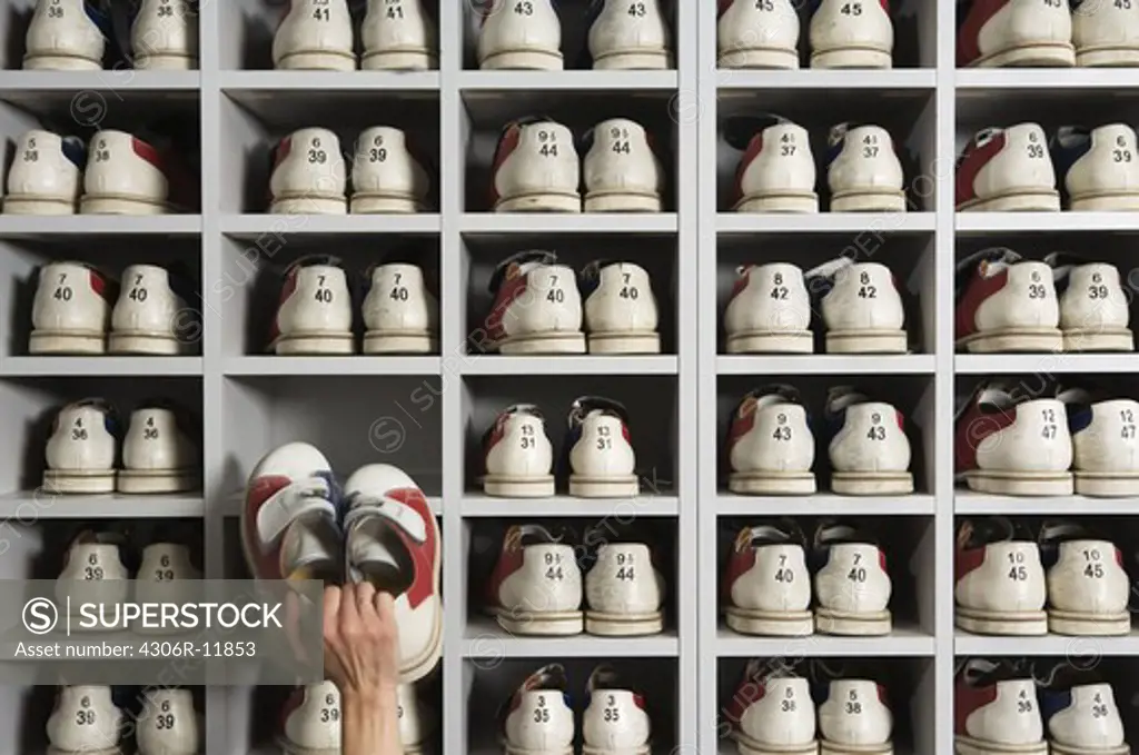 Hand picking shoes on shelves in a bowling alley.
