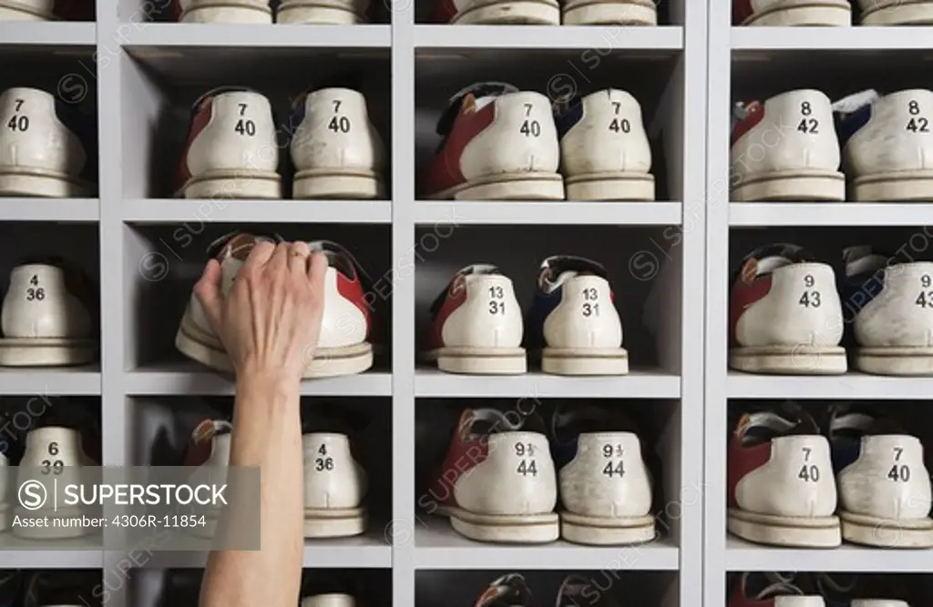 Hand picking shoes on shelves in a bowling alley.