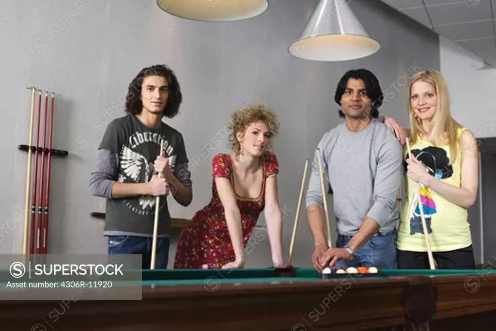 Four people standing by a pool table.
