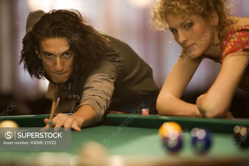 A man playing pocket billiards, a friend is watching.