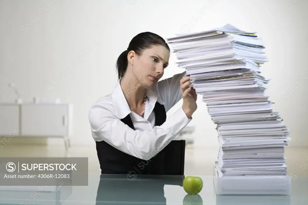A woman in an office with a large pile of paper.